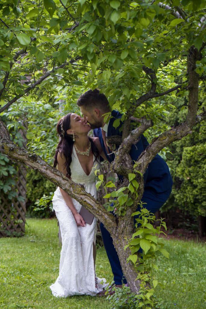 Bride and groom kissing between leafy branches.