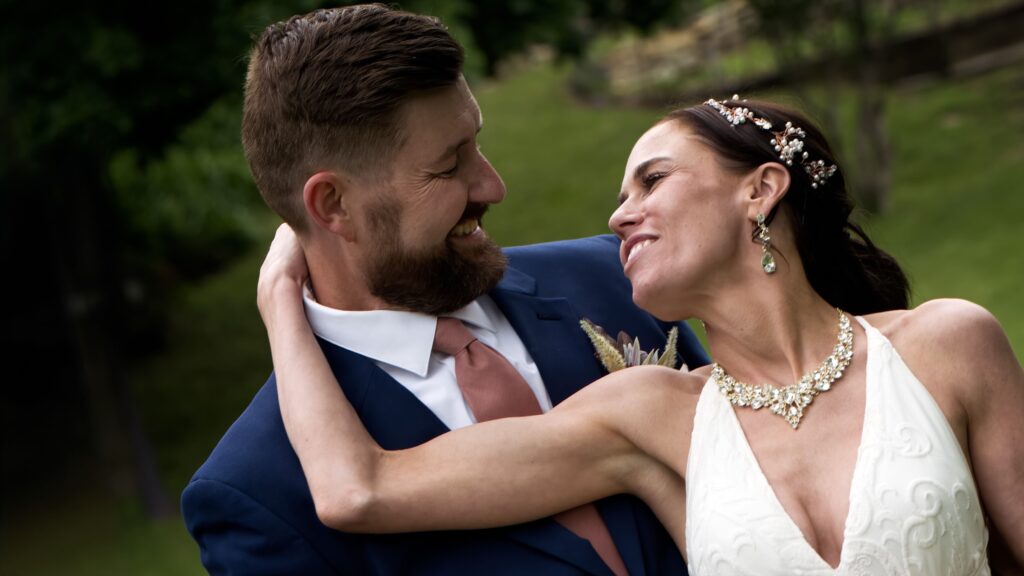 A couple smiling at each other in a close outdoor portrait.