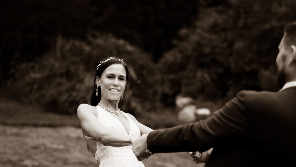 Black-and-white photograph of a bride smiling as she holds her groom’s hand outdoors.