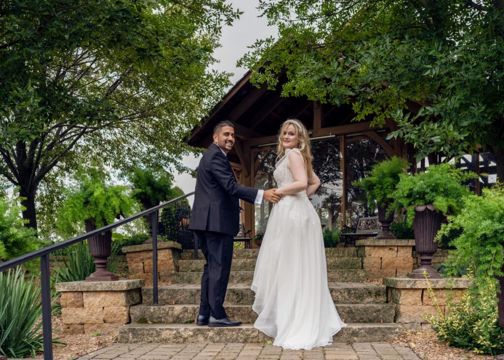 Newlyweds holding hands on garden steps.