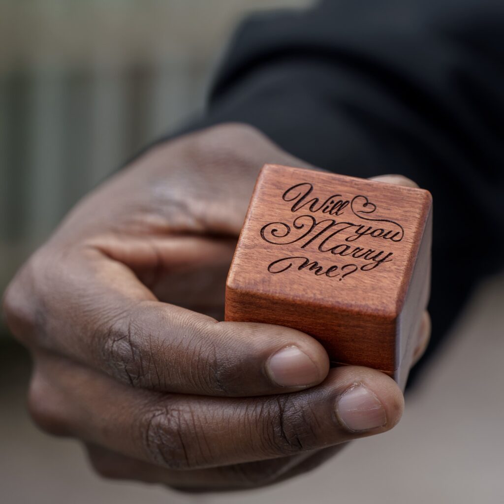 A wooden ring box with the words Will You Marry Me held in one hand.