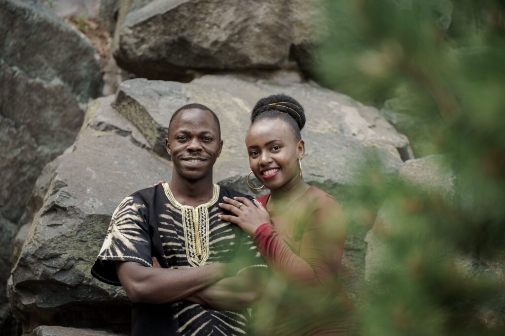 A couple sitting together among large rocks and green foliage.