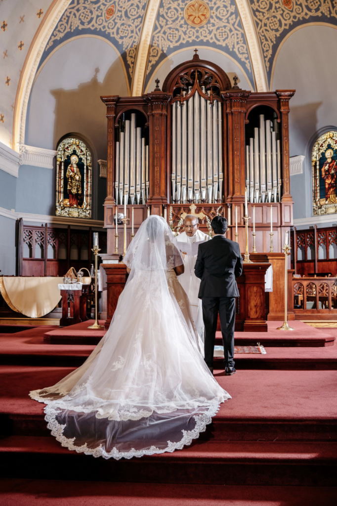 Bride and groom in a church aisle beneath an organ loft.