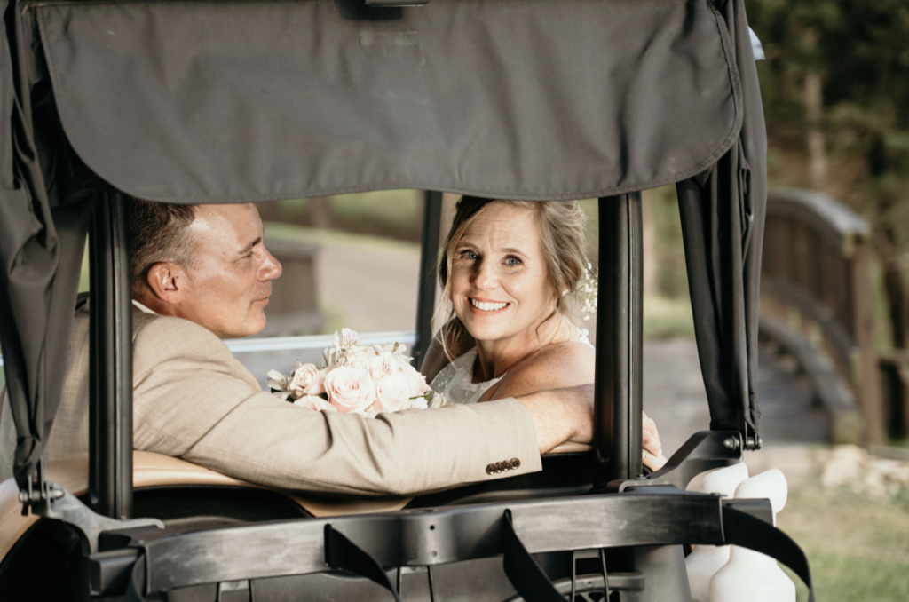 Bride and groom smiling from a golf cart.