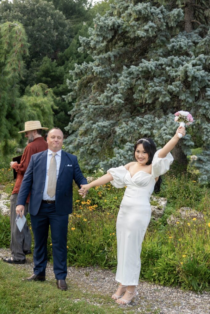 Newlyweds celebrating with their hands raised after an outdoor ceremony.