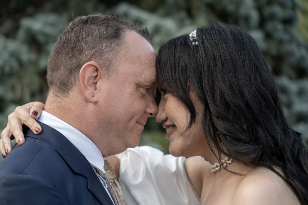 Bride and groom touching foreheads in a close garden portrait.