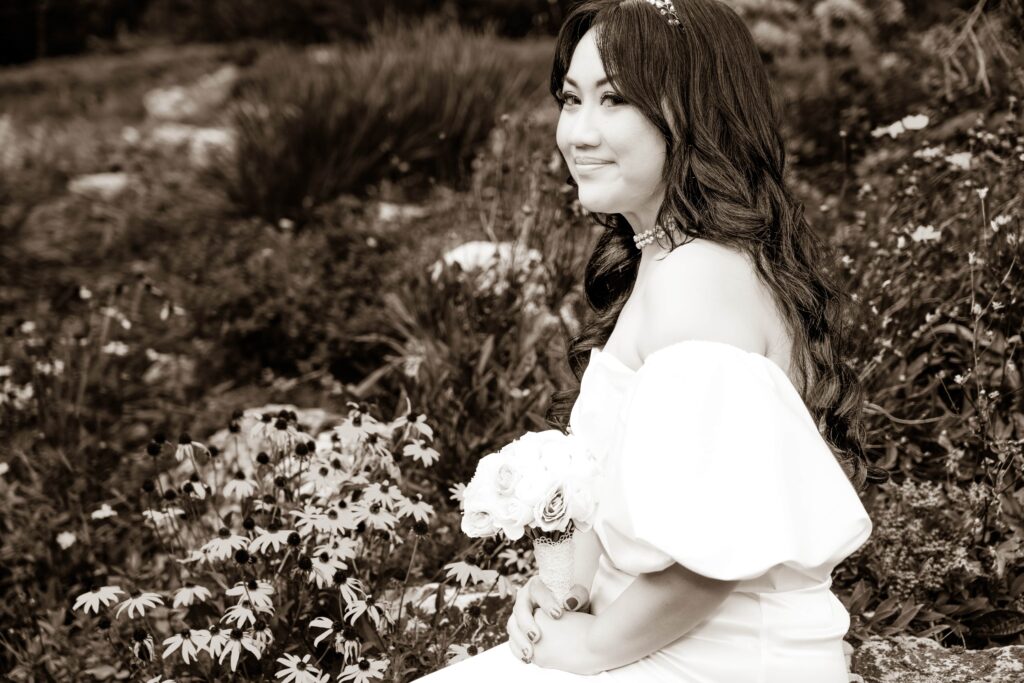 Bride holding her bouquet beside leafy plants.