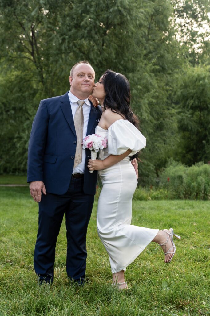Bride kissing the groom on the cheek while lifting one foot.