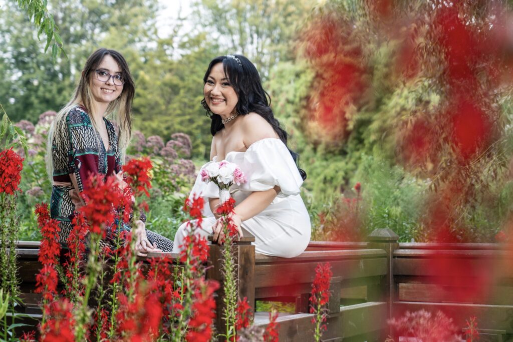 Bride smiling with a guest beside bright flowers.